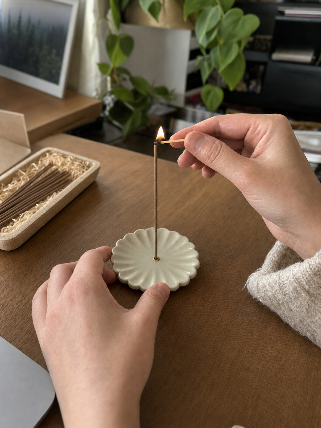 Hands lighting a Hourstick incense stick in the chrysanthemum ceramic holder with a wooden match