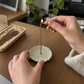 Hands lighting a Hourstick incense stick in the chrysanthemum ceramic holder with a wooden match